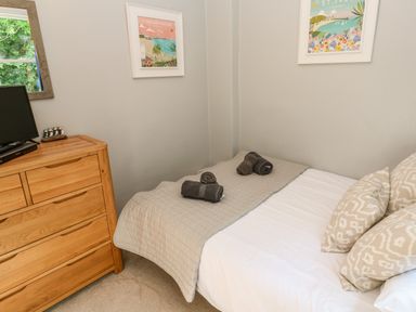 A bedroom with a wood dresser a bed with pillows and folded towels on a blanket at 8 Rosewall Cottages in St Ives