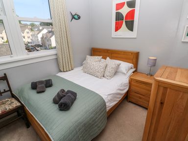 A bedroom with a wooden bed with green bedspread and patterned pillows a bedside table with lamp and a wooden chest of drawers at 8 Rosewall Cottages in St Ives