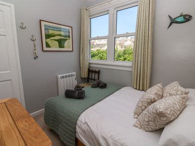 A bedroom with a bed pillow and blanket near a window with curtains and a wooden chair at 8 Rosewall Cottages in St Ives