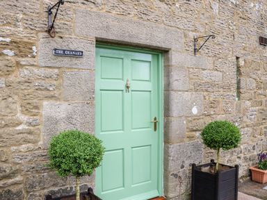 A green door set in a stone wall with two potted topiary bushes on either side at The Granary in Longwitton near Morpeth