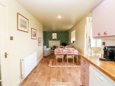 A kitchen and dining area with wooden flooring and pink cabinets with a dining table and chairs at The Granary in Longwitton near Morpeth