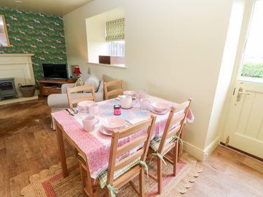 A dining table set with pink dishes and cups in a room with wooden chairs and a door at The Granary Longwitton near Morpeth