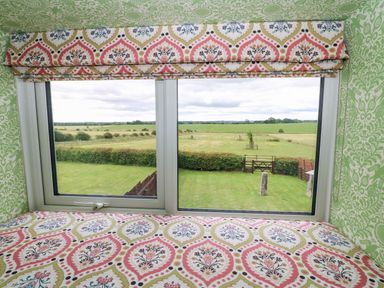 A window with floral patterned valance and seat cushion overlooking a green field at The Granary in Longwitton near Morpeth