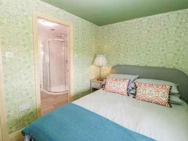 A bedroom with a bed bedside table and lamp next to a door leading to a shower at The Granary in Longwitton near Morpeth