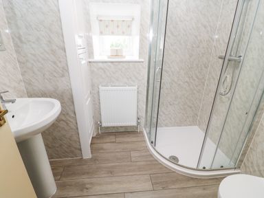 A bathroom with a shower enclosure a sink a small window with a floral blind and a radiator at The Granary in Longwitton near Morpeth