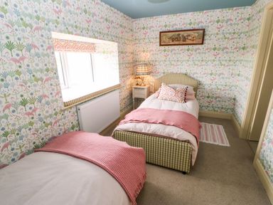 A bedroom with two single beds a nightstand with a lamp a window and patterned wallpaper at The Granary in Longwitton near Morpeth