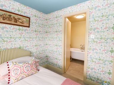 A bedroom with patterned wallpaper a bed with cushions and an open door revealing a bathroom with a bathtub at The Granary in Longwitton near Morpeth
