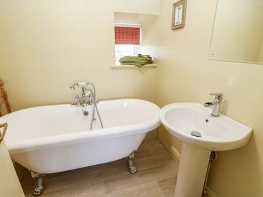 A bathroom with a clawfoot bathtub pedestal sink and a small window with green towels at The Granary in Longwitton near Morpeth