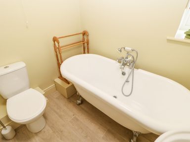 A bathroom with a white toilet a white clawfoot bathtub a wooden towel rack and a window with towels at The Granary in Longwitton near Morpeth