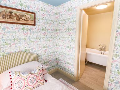 A bedroom with patterned wallpaper and a bed with pillows next to a doorway leading to a bathroom with a bathtub at The Granary Longwitton near Morpeth