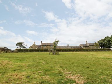 A stone farmhouse with outbuildings surrounded by a fenced grass field at The Granary in Longwitton near Morpeth