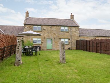 A backyard with green grass a table umbrella and chairs in front of a stone house at The Granary in Longwitton near Morpeth