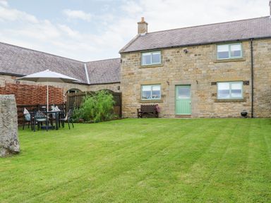 A garden with a table and chairs under an umbrella and a stone house with green windows and door at The Granary in Longwitton near Morpeth