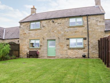 A stone house with mint green windows and door a bench and grill in the yard at The Granary in Longwitton near Morpeth