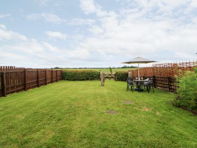 A grassy backyard with a wooden fence and outdoor table with umbrella at The Granary in Longwitton near Morpeth