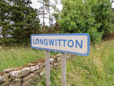 A roadside sign with longwitton on it with trees and grass behind at The Granary in Longwitton near Morpeth