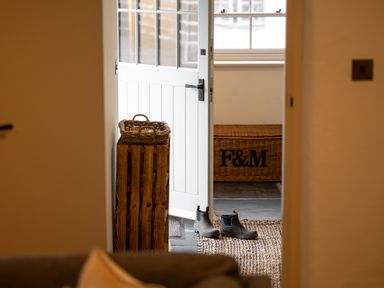 An open white door with rubber boots on a rug and a wicker basket in a hallway at The Lodge in Newby Bridge