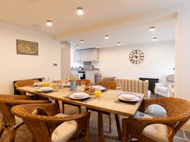 A dining area with a wooden table set with dishes and wicker chairs in an open plan kitchen and living space at The Lodge in Newby Bridge