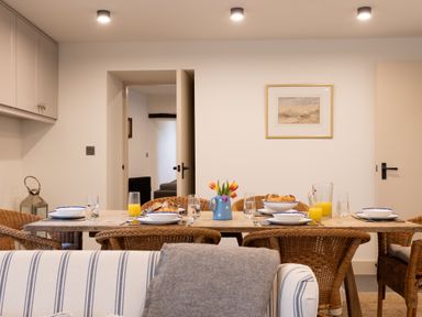 A dining room with a wooden table set with plates glasses jug of orange juice and a vase with flowers at The Lodge in Newby Bridge