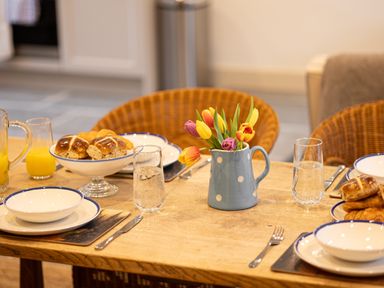 A dining table with bowls plates glasses of water and orange juice bread and a vase with tulips at The Lodge in Newby Bridge