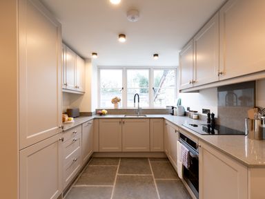 A kitchen with cream cabinets a sink under a window and an oven on the right at The Lodge in Newby Bridge