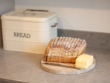 A sliced loaf of bread with a block of butter and a butter knife on a wooden board on a kitchen counter with a bread box in the background at The Lodge in Newby Bridge