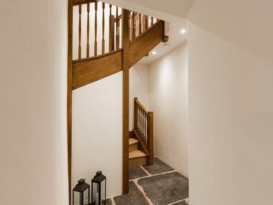 A hallway with a wooden staircase and two black lanterns on the stone floor at The Lodge in Newby Bridge