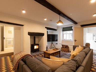 A living room with a gray sofa, a wooden coffee table, a lit wood stove, and a television at The Lodge in Newby Bridge