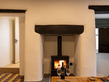 A wood burning stove with fire inside and a bottle of wine with two glasses on a wooden table at The Lodge in Newby Bridge
