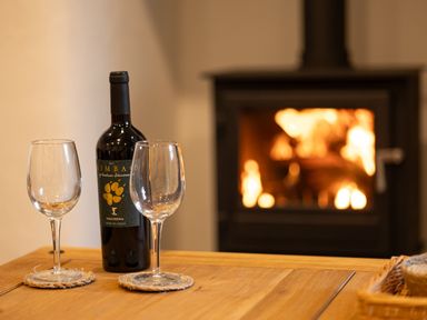A bottle of wine and two empty glasses on a wooden table in front of a lit fireplace at The Lodge in Newby Bridge