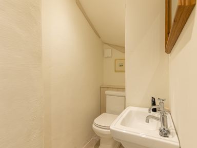 A small bathroom with a toilet and a sink with twin taps and a wooden framed mirror above the sink at The Lodge in Newby Bridge