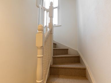 A carpeted staircase with white banisters and a window at The Lodge in Newby Bridge
