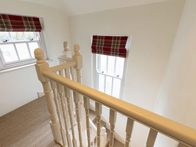 A staircase with white wooden railing and two windows with plaid red and beige blinds at The Lodge in Newby Bridge