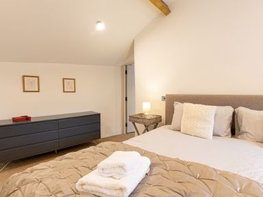 A bedroom with a bed and folded towels on it a black dresser against the wall and a side table with a lamp at The Lodge in Newby Bridge