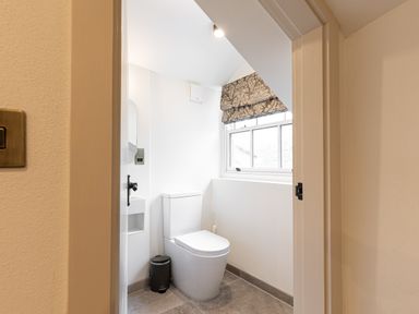 A small bathroom with a toilet a trash bin a window with patterned blinds and a mirror on the wall at The Lodge in Newby Bridge