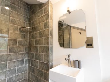 A bathroom with stone tile walls a sink mirror and a soap dispenser at The Lodge in Newby Bridge
