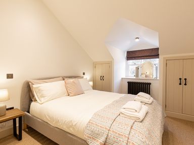 A bedroom with a bed towel and pillows a wooden side table window with a radiator and wardrobes at The Lodge in Newby Bridge