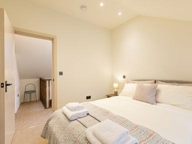 A bedroom with a bed folded towels bedside lamp and chair near a staircase at The Lodge in Newby Bridge