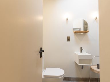 A small bathroom with a toilet a wall-mounted sink a round mirror and a small table with a cup at The Lodge in Newby Bridge