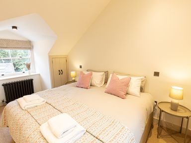 A bedroom with a large bed two bedside tables with lamps a window with a blind and a small cupboard at The Lodge in Newby Bridge