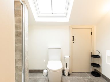 A bathroom with a toilet a toilet brush holder a toilet paper holder a door and a black three tier shelf at The Lodge in Newby Bridge