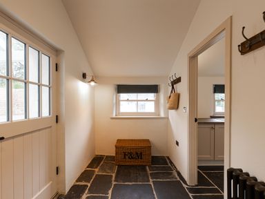 A hallway with a basket under a window and wall hooks near a door at The Lodge in Newby Bridge