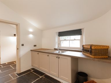 A kitchen area with cabinets a sink a window and a wicker basket on the counter at The Lodge in Newby Bridge
