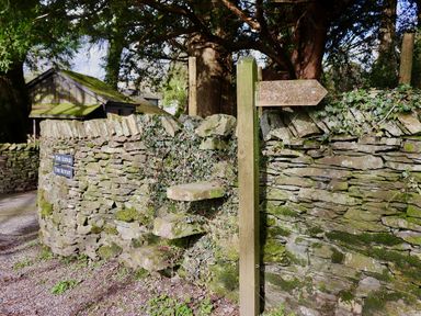 A stone wall with a wooden signpost and stone steps at The Lodge in Newby Bridge