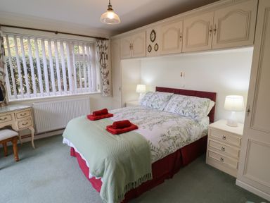 A bedroom with a bed with floral bedding and red towels on top with bedside tables and lamps at Woodstock in Chaffcombe near Chard
