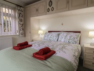 A bedroom with a bed and red towels on it two bedside tables with lamps and a window with curtains at Woodstock in Chaffcombe near Chard