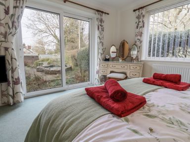 A bedroom with a bed and red towels near a window and a dressing table at Woodstock in Chaffcombe near Chard