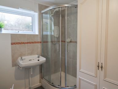 A bathroom with a corner shower enclosure a wall-mounted sink and a window at Woodstock in Chaffcombe near Chard