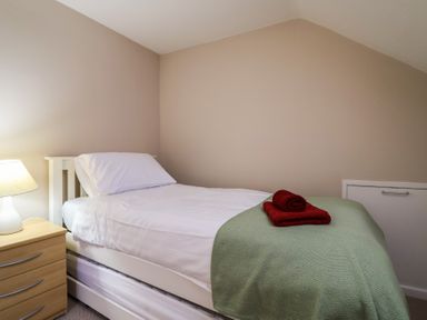 A bedroom with a single bed with white sheets and green cover with red towels on top and a nightstand with a lamp at Woodstock in Chaffcombe near Chard