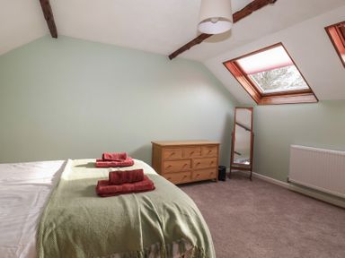 A bedroom with a bed, folded towels, a wooden chest of drawers, a full length mirror, and skylight windows at Woodstock in Chaffcombe near Chard